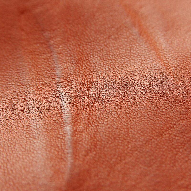 Extreme macro close-up of terracotta-orange leather showing a central fold or crease with fine pebble grain texture visible across the entire surface